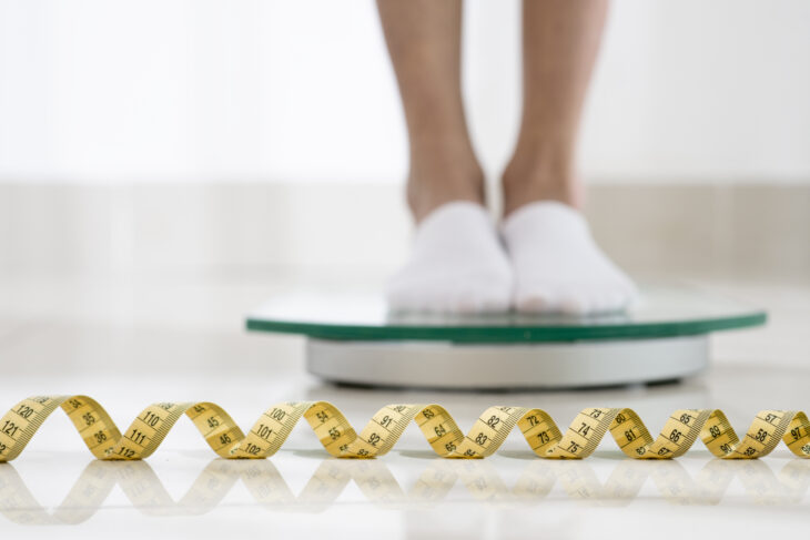 Legs standing on a scale with a measuring tape in the foreground