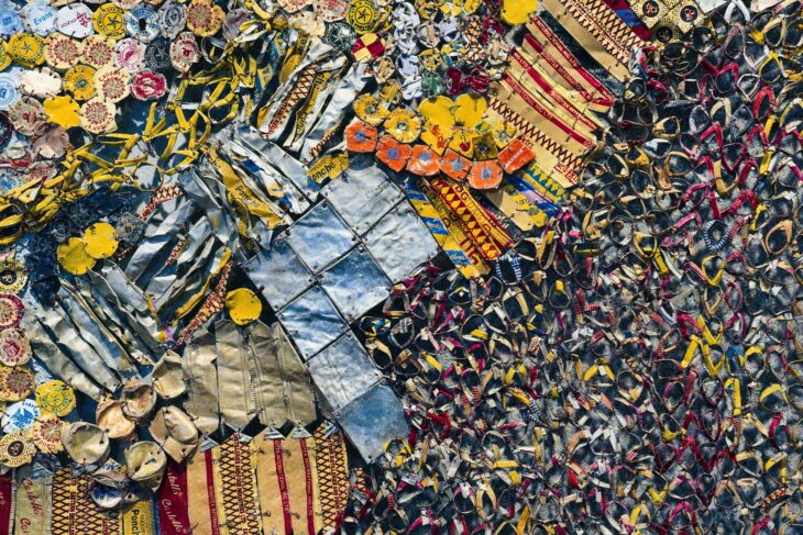 A Detailed Close-Up of a Colorful Mosaic Wall Made From Recycled Materials - A close-up shot of a colorful mosaic wall created from recycled materials. The wall is composed of various pieces of metal, fabric, and other materials, all stitched together to form a complex and intricate pattern. The colors are bright and vibrant, creating a visually stunning and textured surface.